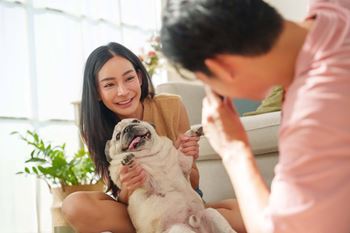 A woman is sitting on a couch with a dog, and a man is standing beside her holding a remote control  at Spyglass Hill Apartments, Bremerton, 98337